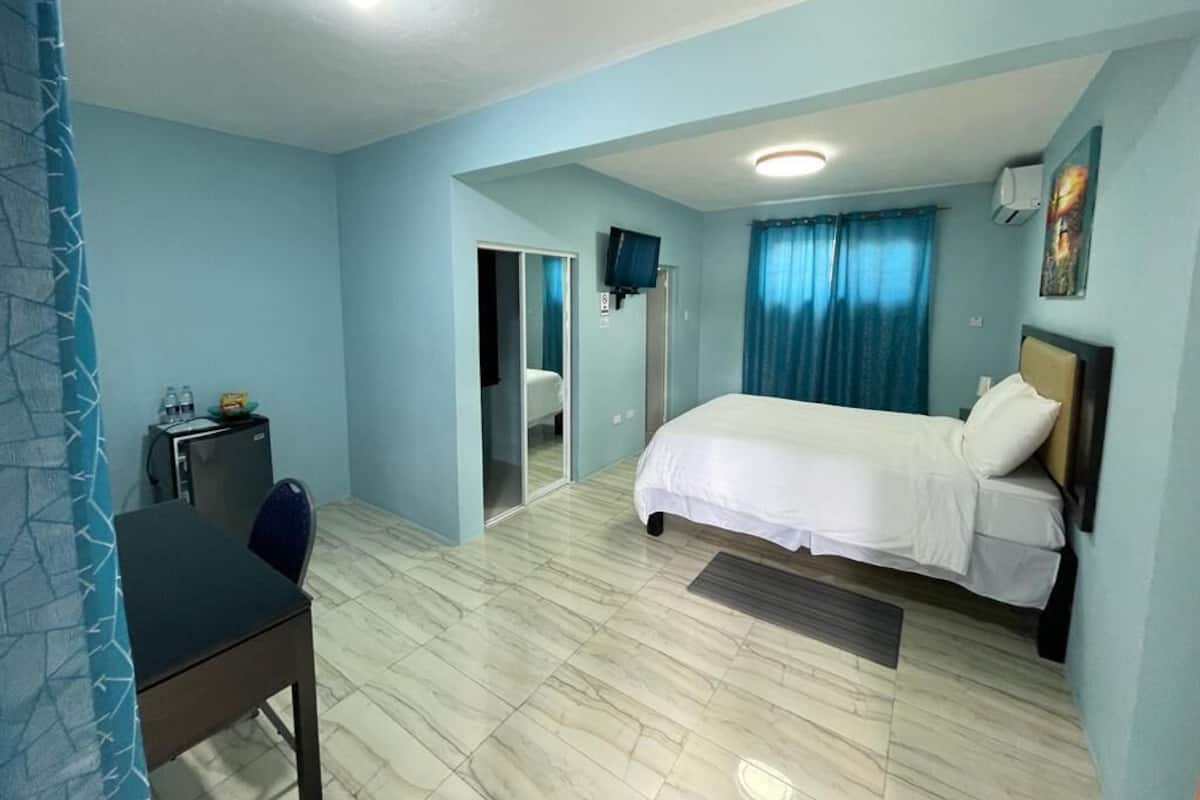 Ein Schlafzimmer mit Bett, Schreibtisch, Stuhl, Fernseher und einem durchgegangenen Tür einsehbaren Badezimmer.
