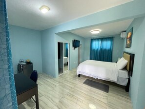 A bedroom with a bed, a desk, a chair, a television, and a bathroom visible through an open door.