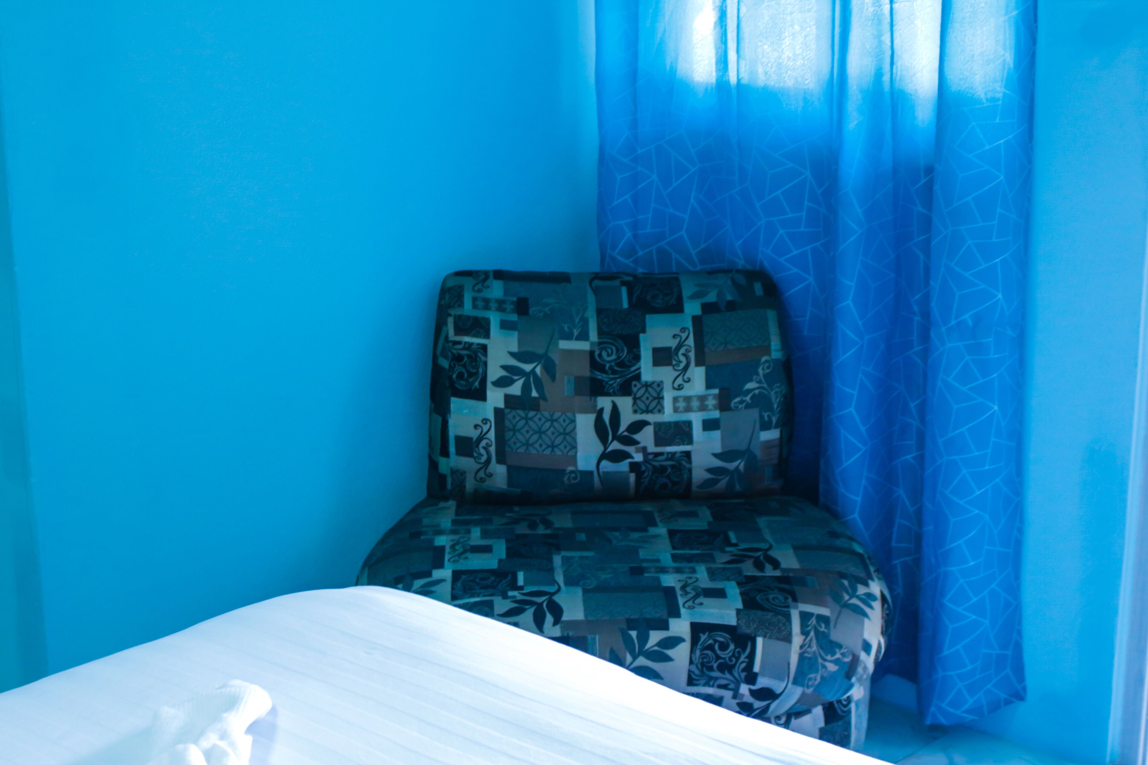 A room with a bed, a patterned armchair, and blue curtains.