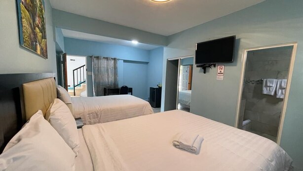 A hotel room with two beds, a television, a shower, and a painting on the wall. - Ocean View Beach Hotel (Ocho Rios)