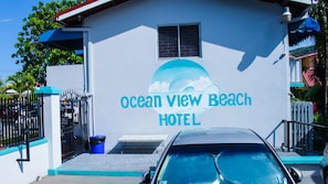 The exterior of Ocean View Beach Hotel with a clear view of the entrance, a blue trash bin, and a car parked in front.