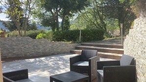 An outdoor patio with wicker furniture, stone steps, and a view of trees and hills. - Lovely 2-room apartment in the heart of Esterel with swimming pool (Les Adrets-de-l'Estérel)