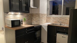 A compact kitchen with dark cabinets, a microwave, a stove, a sink, and a window overlooking the outside. - Lovely 2-room apartment in the heart of Esterel with swimming pool (Les Adrets-de-l'Estérel)
