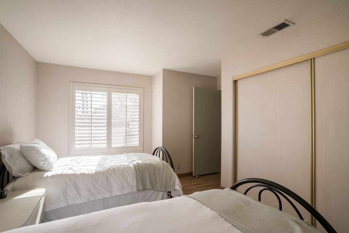 Une chambre avec deux lits, une fenêtre avec des stores, une porte et une armoire.