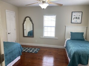A bedroom with two beds, a ceiling fan, a window, and a door.