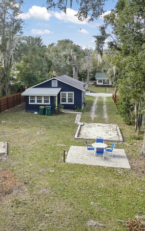 A backyard with a blue house, a patio with blue chairs, and a wooden fence.
