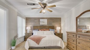 Un dormitorio con una cama, dos mesitas de noche, un tocador, un ventilador de techo y un espejo grande.