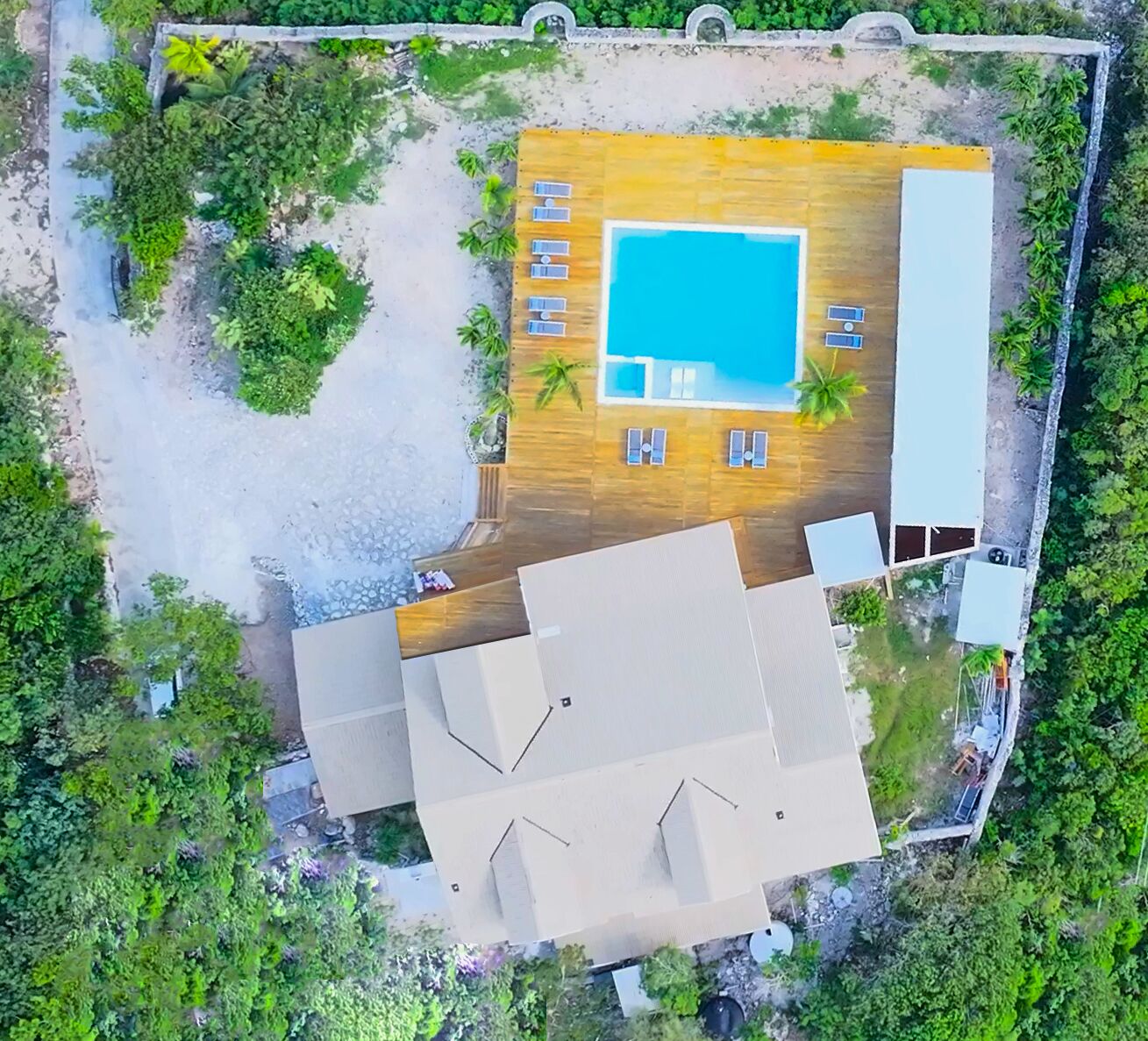 An aerial view of a resort with a swimming pool, sun loungers, and a wooden deck area.