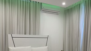 Une chambre moderne avec un grand lit, des rideaux blancs, une table de chevet avec une plante et un appareil de climatisation.