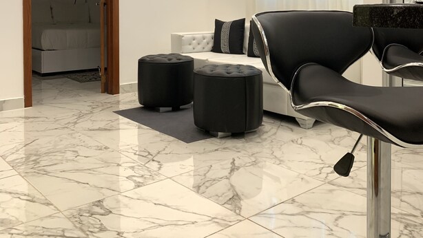 Une chambre moderne avec un fauteuil en cuir noir, deux poufs, un canapé blanc et un lit à l’arrière-plan.