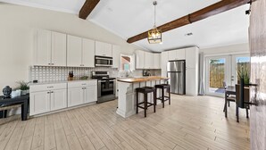 A spacious kitchen with white cabinets, a wooden island, and a large window. - Beach Side Destin Retreat (Destin)