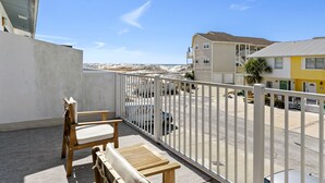 A balcony with a wooden chair and table, overlooking a parking area and buildings with a clear view of the beach. - Beach Side Destin Retreat (Destin)