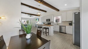 A modern kitchen with white cabinets, a central island with stools, a built-in oven, and a stainless steel refrigerator. - Beach Side Destin Retreat (Destin)
