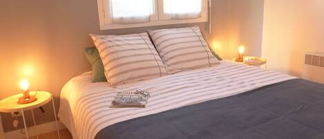 Una cama bien hecha con ropa de cama a rayas, dos lámparas de noche y una revista sobre la cama.