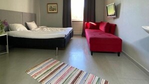 Une chambre à coucher avec un lit, un canapé rouge, une télévision et une fenêtre avec des rideaux.