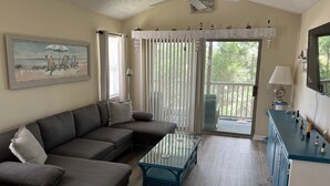 Una sala de estar con un sofá modular, una mesa de centro de vidrio, un ventilador de techo y vistas al exterior a través de una puerta corrediza de cristal.