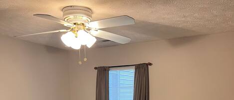 A bedroom with a bed, a ceiling fan, a window with curtains, a bedside table, and a TV.