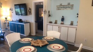 Un comedor con una mesa redonda, sillas de mimbre blanco y mantel azul turquesa.