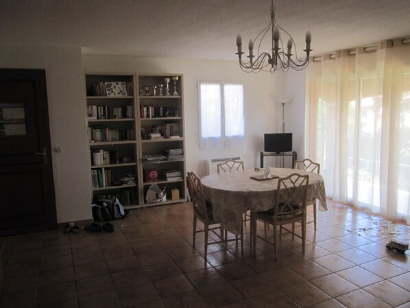A dining area with a round table and chairs, a bookshelf, a television, and a door.