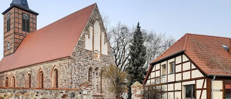 A historic church with a prominent tower and a traditional half-timbered house adjacent to it.