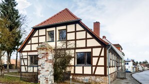 A traditional half-timbered house with a tiled roof, a stone pillar, and a gated entrance.