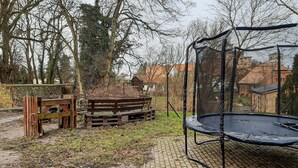 A trampoline in a backyard with a wooden bench and a fence.