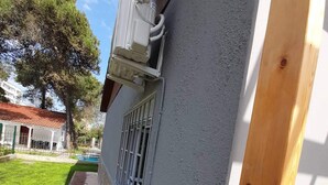 Ein Gebäude mit grauem Anstrich, einem Holzbalken rechts und einem Fenster mit Metallgitter.