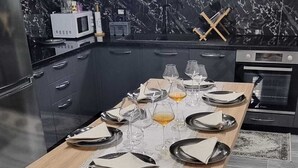 Eine moderne Küche mit dunklen Schränken, einer Marmor-Spritzschutzwand und einem Esstisch, gedeckt für sechs Personen, mit Gläsern und Tellern.