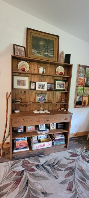 A wooden bookshelf with framed photos and books, a decorative plate, and a painting above it. - Cozy new built home for 2, country living with city near by (West Olive)