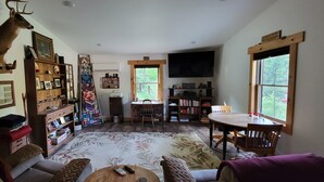 Un salon chaleureux avec une cheminée, une tête de cerf accrochée au mur, une bibliothèque, un téléviseur et un coin repas avec une table et des chaises.