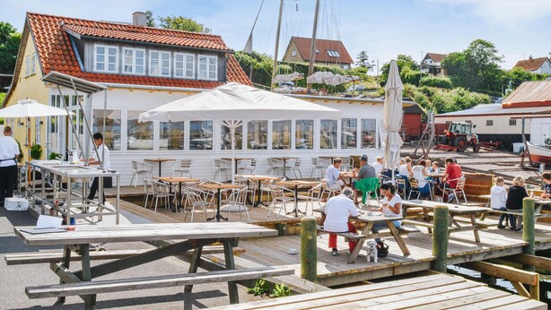 A waterfront restaurant with outdoor seating, a covered dining area, and a view of the water.