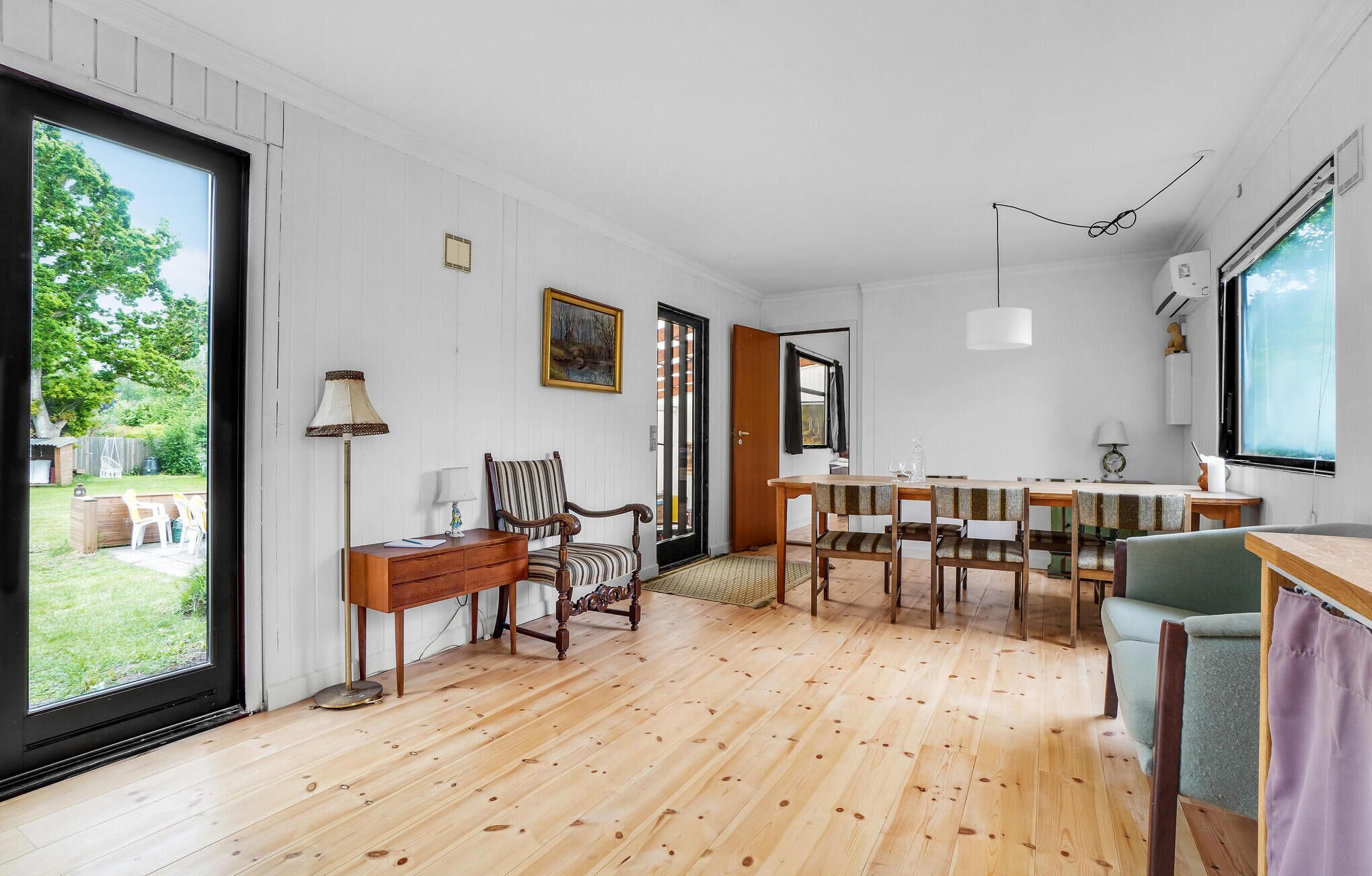 A spacious kitchen with wooden flooring, a dining area with striped chairs, and a large window providing a view of the outdoors.
