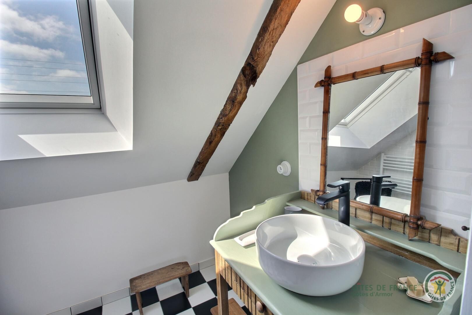 A modern bathroom with a skylight, a large mirror, and a bowl sink.
