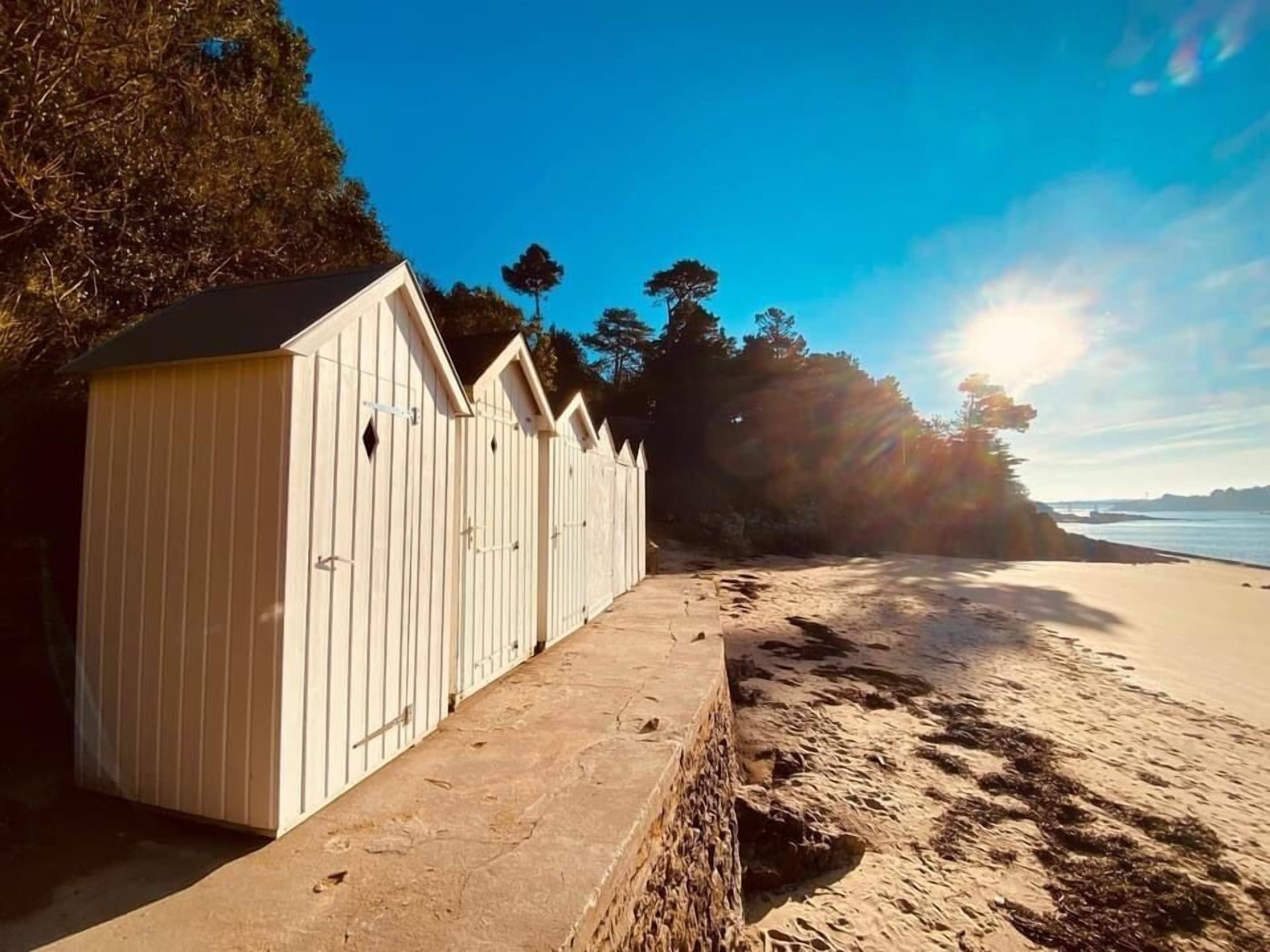 A row of white beach huts with a stone pathway leading to the beach.