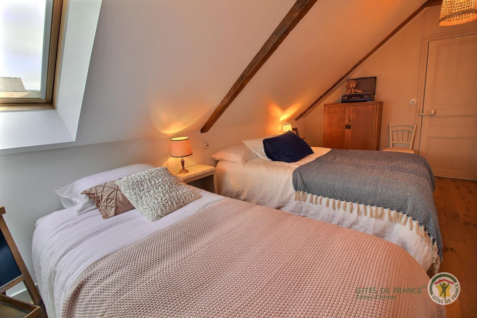 Een knus slaapkamer met twee bedden, een houten plafond en een klein kastje.