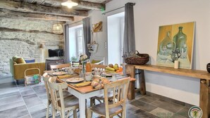 Un coin repas agrémenté d’un mur en pierre rustique, de poutres en bois au plafond et d’une table dressée pour quatre personnes.