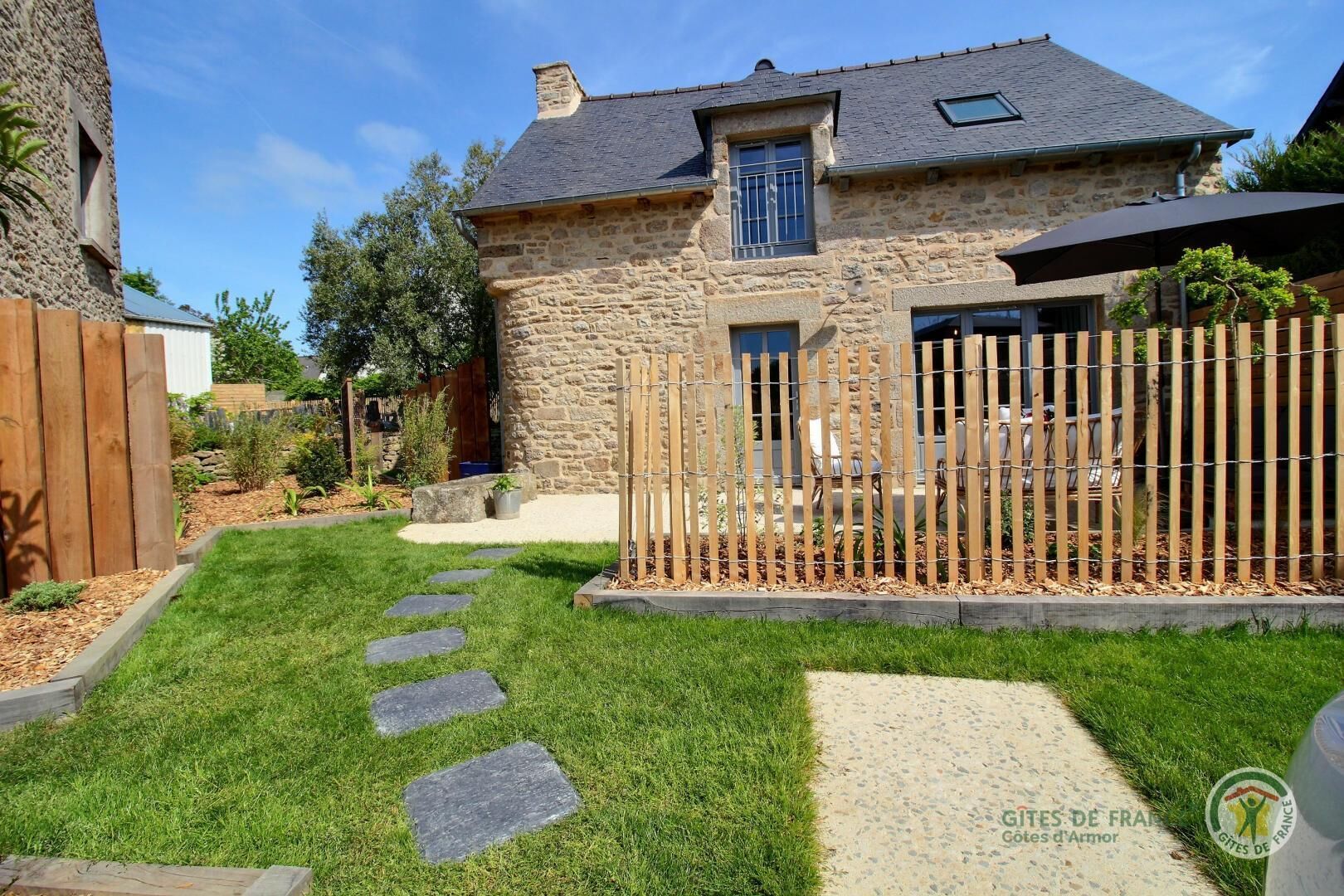 Una casa de piedra con cerca de madera, un sendero empedrado y un césped.