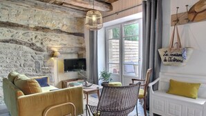 Une pièce chaleureuse avec un mur en pierre, un canapé, un fauteuil en osier et un téléviseur fixé au mur.