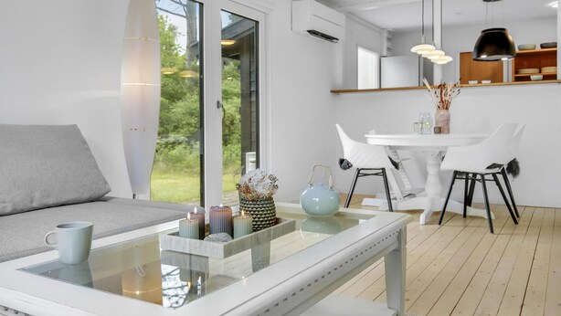 A modern living room with a glass coffee table, a grey sofa, and a dining area with white chairs and a white table. - 2 bedroom cozy home in Dronningmølle (Dronningmølle)