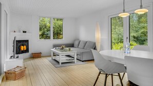 A modern living room with a fireplace, a grey sofa, a white coffee table, and a dining area with a white table and chairs. - 2 bedroom cozy home in Dronningmølle (Dronningmølle)