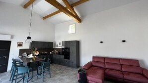 A spacious living area with a red sofa, a dining table with chairs, a kitchen with dark cabinets, and a wooden ceiling structure.