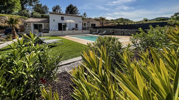 A modern house with a swimming pool, surrounded by lush greenery and a clear blue sky.