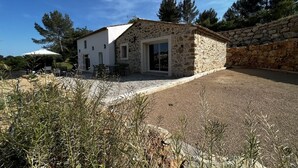 A stone house with a white exterior, a patio with outdoor furniture, and a stone wall in the background.