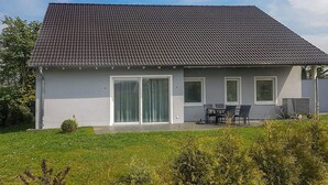 Et toetagers hus med grå tagsten, en overdækket terrasse med udendørs møbler og en græsplæne.