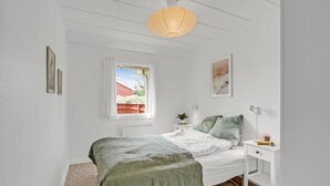 Quarto com cama, mesa de cabeceira, janela com vista para um celeiro vermelho e luminária pendente.