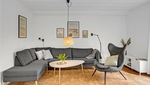 Uma sala de estar moderna com um sofá seccional cinza, uma mesa de centro redonda com uma planta, uma cadeira única e quadros nas paredes.
