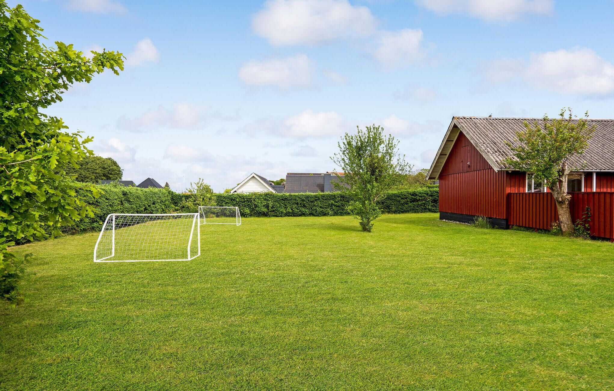 A well-maintained grassy area with a soccer goal, surrounded by a red barn and a hedge.