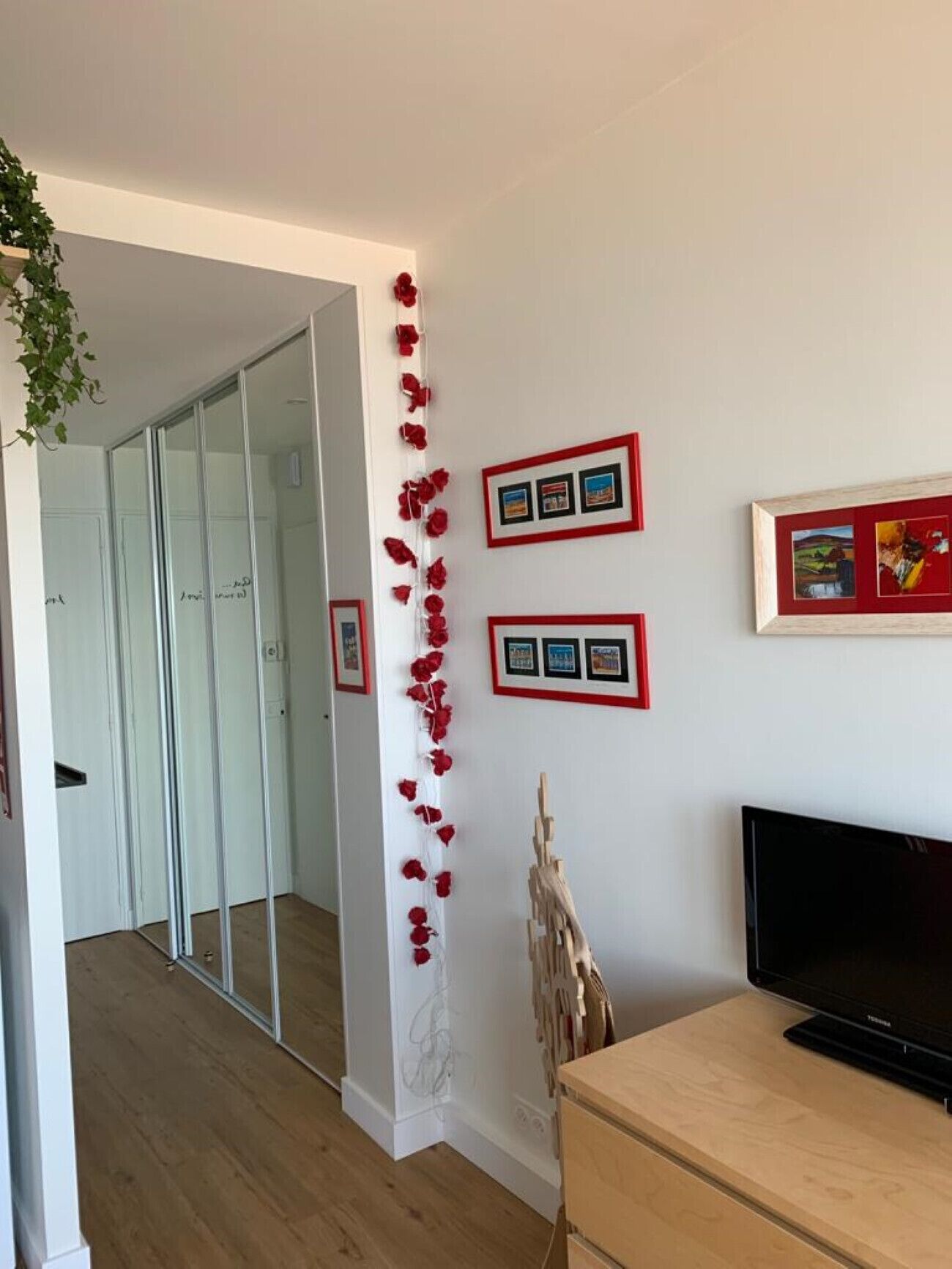 Een moderne woonkamer met een flatscreen televisie, ingelijste foto’s aan de muur en een decoratief bloemarrangement rood.