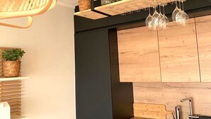 A modern kitchen with black cabinetry, a wooden countertop, and a built-in oven. There are hanging wine glasses and decorative jars on the shelf above the sink.