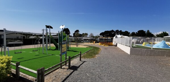 Un parque infantil con columpios, una estructura para escalar y una zona vallada con un tobogán.
